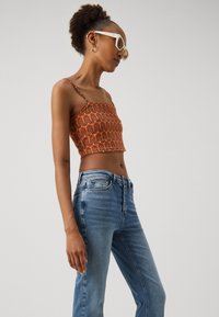 Top corto arancione con motivo a onde e spalline sottili abbinato a jeans a vita alta di colore azzurro chiaro, dotati di chiusura a bottone e leggero sbiadimento.
