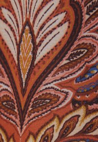 Gros plan sur un tissu avec un motif cachemire complexe dans des tons orange, marron, crème et bleu.