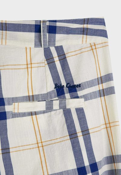Gros plan sur un tissu beige à motif à carreaux bleu et jaune, montrant une boucle de ceinture à la taille, une poche fendue et un texte de marque brodé.