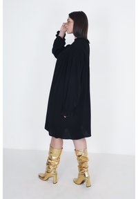 Zwarte lange mouwen jurk met gerimpelde manchetten, voorzien van een textuur in de schouderpartij. Gecombineerd met slouchy metallic gouden laarzen tot de knie met blokhakken.