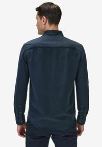 Mörkblå långärmad skjorta i bomullstyg, med knappslå och justerbara ärmslut. Slät textur och rundad nederkant.
