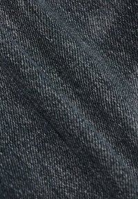 Gros plan sur un tissu en denim bleu foncé montrant une texture de tissage en diagonale et des plis subtils.