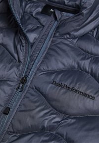Marineblaue isolierte Jacke mit gestepptem Design, ausgestattet mit einem Reißverschluss vorne und gesticktem "Peak Performance"-Logo auf der linken Seite.