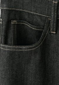 Gros plan sur la poche d’un jean en denim noir avec des coutures beiges et une boucle de ceinture visible en haut à droite.