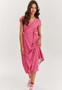 Růžové šaty s krátkým rukávem a květinovým vzorem. Mají zavazovací pas a vzorovaný lem. Nosí se s růžovými teniskami.