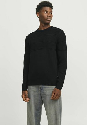 Black knitted sweater featuring textured horizontal patterns, round neck, and ribbed cuffs. Worn with light blue denim jeans.