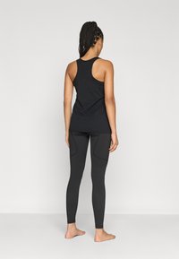 Czarny top na ramiączkach typu racerback w połączeniu z obcisłymi czarnymi legginsami z bocznymi kieszeniami i gładką fakturą.