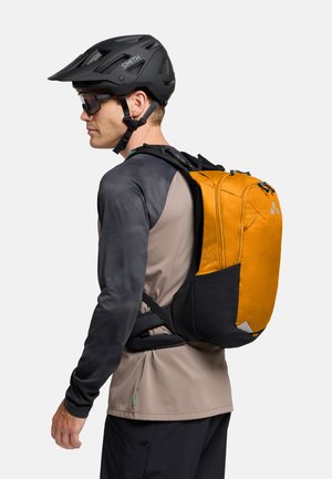 Zaino arancione con accenti neri, caratterizzato da un design elegante e cerniere. Casco nero e occhiali indossati dall'individuo. Maglietta grigia e nera.