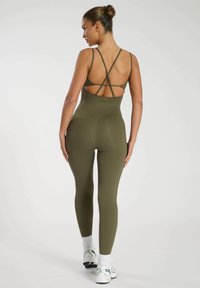 Olivgrön jumpsuit med en kroppsnära design, justerbara tunna axelband och utskärningsdetalj på baksidan. Slät yta, elastiskt material.