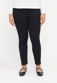 Svarte skinny jeans med en frynsete kant og en jevn tekstur, kombinert med svarte flate sko med en stropp over toppen.