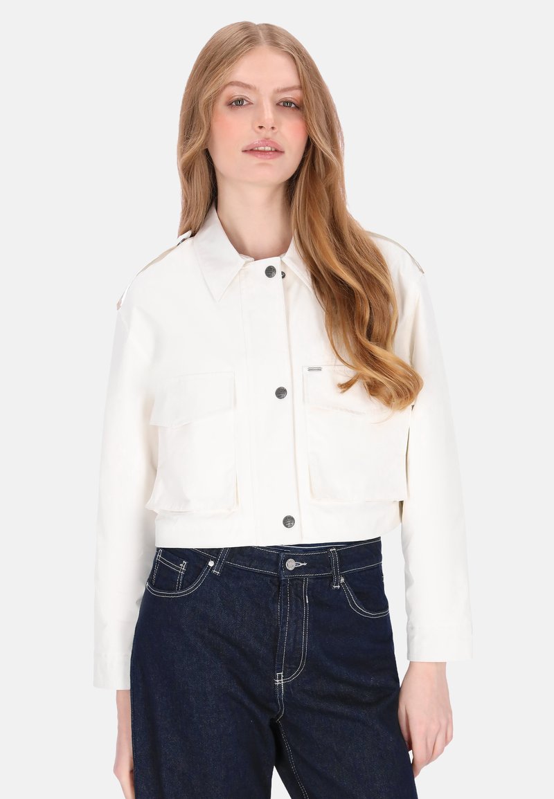 Witte cropped jas met een kraag, twee zakken aan de voorkant en een knoopsluiting. Gecombineerd met donkere denim jeans, gladde textuur.