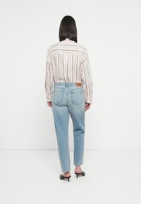 Stripet bluse med løs passform og lange ermer, sammen med lyseblå innsnevrede jeans med midjepute og baklommer. Svart hæler.