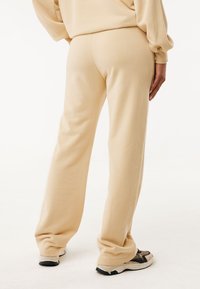 Béžové tepláky, měkká tkanina, volný střih, mírně rozšířená nohavice, s hladkým povrchem a elastickým pasem. V kombinaci s objemovými teniskami.