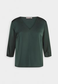Blusa in satin verde scuro con scollo a V e maniche a tre quarti. Texture morbida e superficie liscia, presenta un'etichetta sul collo.