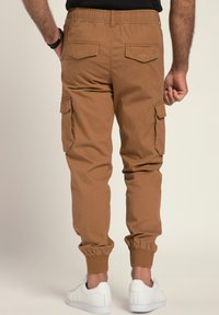 Braune Cargo-Hosen mit elastischem Bund und Bündchen, ausgestattet mit seitlichen und hinteren Taschen. Kombiniert mit weißen Sportschuhen.