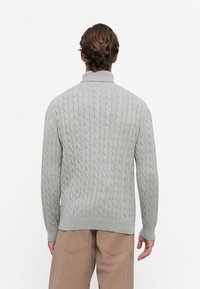 Grauer kabelgestrickter Pullover mit hohem Kragen und gerippten Bündchen, der ein strukturiertes Muster hat, das vertikal entlang des Körpers verläuft.