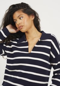 Maglione a righe blu marino e bianche con scollatura a V profonda e colletto. Realizzato in tessuto morbido con una vestibilità rilassata e maniche lunghe.