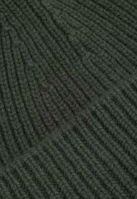 Ciemnozielona dzianina o żebrowanej fakturze z naprzemiennymi wzorami. Włóczka wydaje się miękka i lekko puszysta.