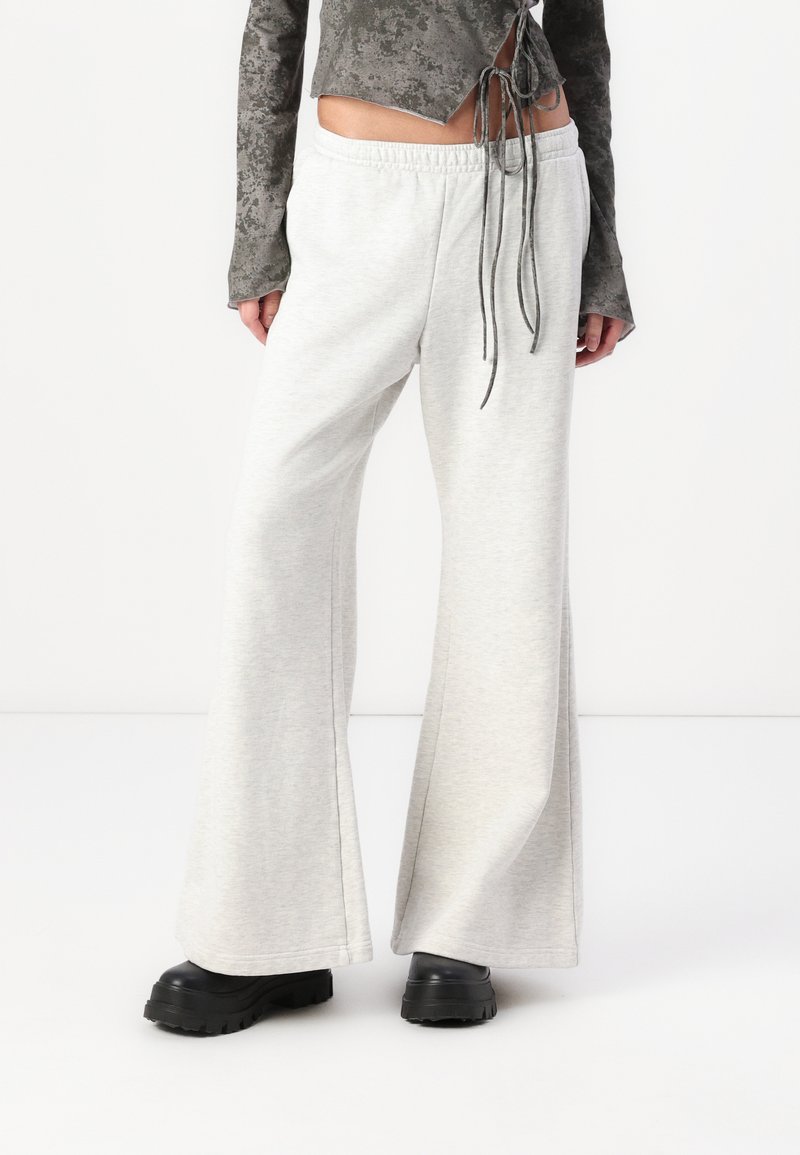 Pantalons de survêtement évasés gris clair en tissu doux, dotés d'une taille élastique et d'une coupe décontractée. Associés à des bottes noires volumineuses.