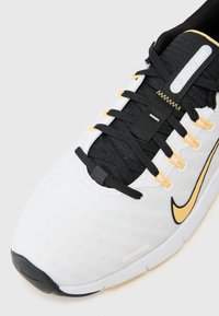 Nike Free 5 sportbačiai balti ir juodi su geltonais akcentais, su orui pralaidžia viršutine dalimi, tekstūruota paviršiumi ir juodomis raištelėmis.