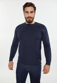 Marineblauwe gebreide trui met een ronde hals en geribbelde manchetten. Bevat een textuurpatroon, een getailleerde vorm en een klein logo-detail aan de onderkant.