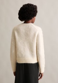 Kremowy, miękki, puszysty sweter z prążkowanym dołem i mankietami; posiada rękawy raglanowe i delikatną strukturę. Widok z tyłu.