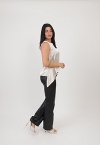 Top senza maniche avorio con un orlo asimmetrico, abbinato a pantaloni neri in ecopelle e sandali bianchi con tacco. Tessuto liscio e lucido.