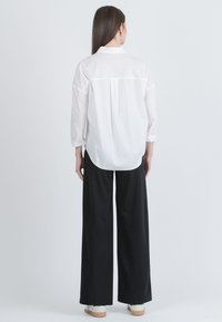 Bílá košile s dlouhými rukávy, s švem na zadním díle. Spárovaná s širokými černými kalhotami a světlou obuví.