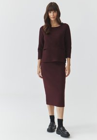 Maglione in maglia bordeaux con maniche a tre quarti abbinato a una gonna lunga fino al ginocchio; presenta un tessuto testurizzato e tasche laterali.