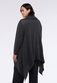 Tmavě šedý oversized svetr s žebrovaným lemem, vysokým límcem a plynulým, asymetrickým tvarem. Měkká textura s jemnými švovými detaily.