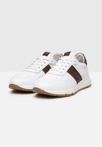 Sneakers bianchi con accenti in pelle marrone. Caratteristiche includono design con lacci, colletto imbottito e suola in gomma per una maggiore aderenza.
