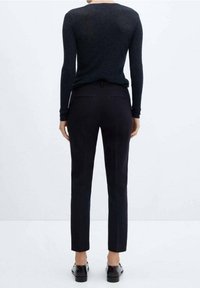 Zwarte geribbelde lange mouw top gecombineerd met op maat gemaakte donkere broek. De broek heeft scherpe plooien en een strakke pasvorm. Zwarte schoenen maken de look af.