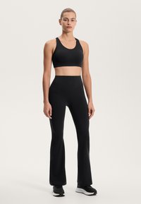 Fekete sportmelltartó széles pántokkal, magas derekú fekete csepp szabású leggingszel párosítva. Sima textúra, minimális design és sportos illeszkedés.