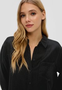 Zwarte katoenen shirt met een textuurafwerking, knoopsluiting aan de voorkant en een enkele borstzak. Heeft een puntige kraag en een losse pasvorm.