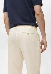 Pantalones de lino amarillos claros con un corte relajado y cinturilla elástica, que cuentan con bolsillos traseros con cierres de botón y sutiles acentos de costura.