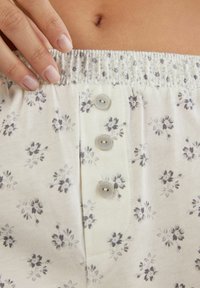 Lichtgekleurde katoenen shorts met een bloemenpatroon, elastische tailleband en drie knopen aan de voorkant. Zachte textuur en ademend ontwerp.