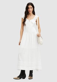 Robe maxi en coton blanc avec des bretelles volantées, un corsage smocké et une jupe à volants. Assortie à des bottines noires avec des accents dorés.