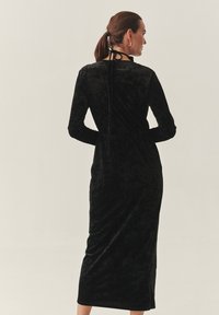 Črna svilena midi obleka z dolgimi rokavi, prilegajočim se siluetom in detajlom za zavezovanje pri vratu. Gladka tekstura in minimalističen dizajn.