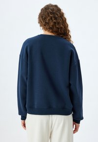 Sudadera azul marina hecha de tejido suave, con un corte relajado, hombros caídos y puños y dobladillo acanalados.