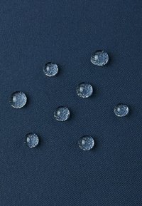 Blauer Stoff mit einer strukturierten Oberfläche, die mehrere klare Wassertropfen mit Reflexionen zeigt, die über das Material verteilt sind.