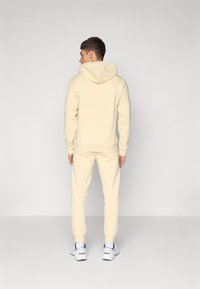Gul hættetrøje med matchende joggers, lavet af blødt stof. Har ribstrikkede manchetter og søm samt en kengurulomme foran.