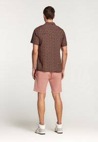 Koszula z krótkim rękawem w ciemnych odcieniach w połączeniu z jasnoróżowymi szortami. Całość dopełniają wygodne sneakersy, koncentrując się na komforcie i odpowiednim dopasowaniu.