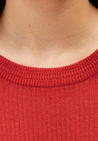 Červený žebrovaný pletený svetr s kulatým výstřihem a jemnou texturou, s pečlivě zpracovanými okraji, které zvýrazňují jeho design.