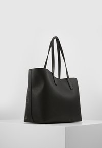 Sort læder tote taske med en tekstureret overflade, struktureret form, dobbelte skulderremme og en diskret branddetalje på siden.