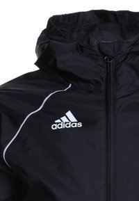 Giacca antivento nera in tessuto liscio. Presenta una chiusura con zip, colletto alto, dettagli bianchi e un logo Adidas sul davanti.