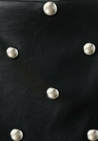 El material de cuero negro presenta tachuelas metálicas plateadas espaciadas regularmente por toda la superficie, creando un diseño texturizado y contrastante.