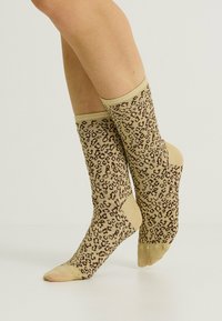 Calcetines hasta la rodilla en beige con un estampado de leopardo marrón. Tejido de punto suave con puños acanalados y refuerzo en la punta y el talón.
