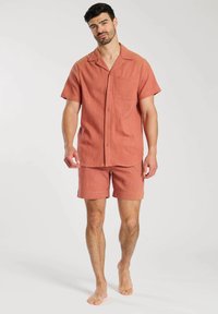 Chemise rouge rouille à manches courtes avec une poche, assortie à un short. Fabriqués dans un tissu texturé, les deux articles ont une coupe décontractée.