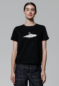 Zwarte katoenen t-shirt met een grafische afbeelding van een astronaut op een wit, hoekig object omringd door sterren. Ronde hals, korte mouwen, ontspannen pasvorm.