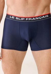 Caleçons boxers bleu marine en tissu texturé, avec une ceinture contrastante noire et rouge arborant le logo "LE SLIP FRANÇAIS".